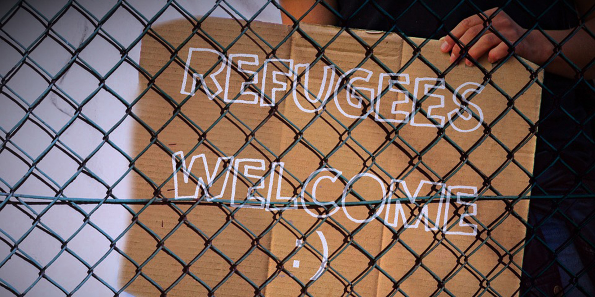 Plakat aus Pappe 'Refugees welcome' hinter einem Zaun