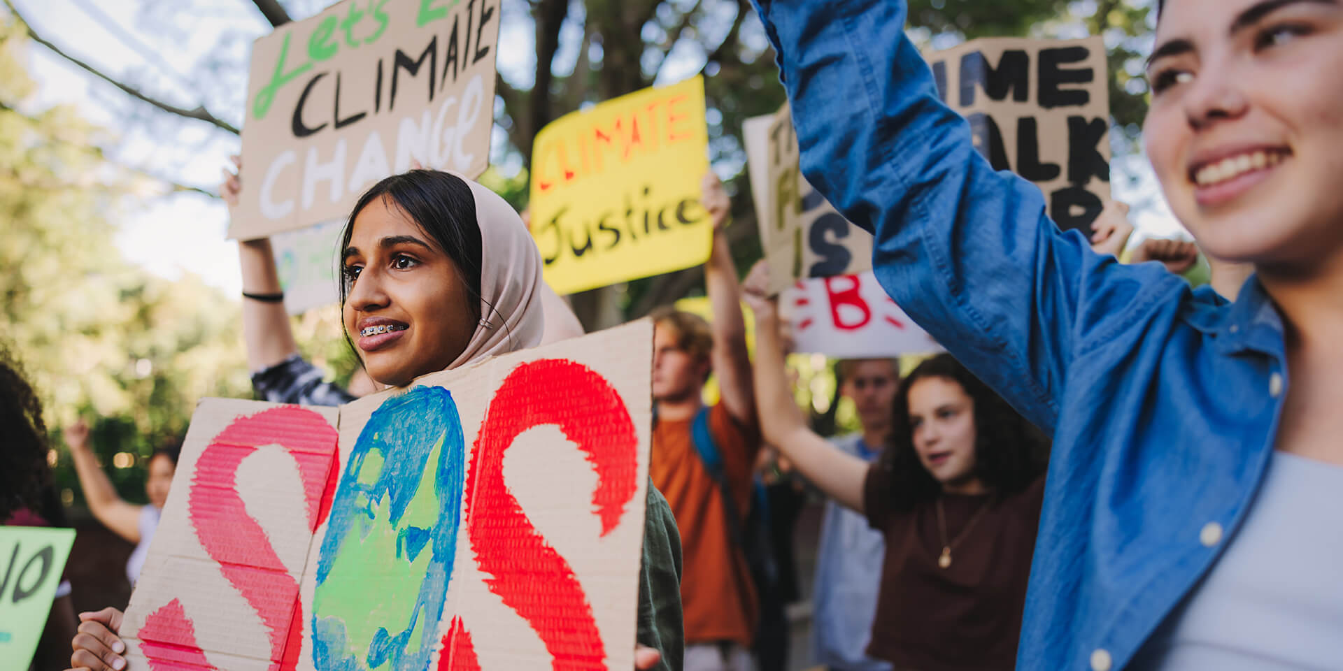  Gruppe multikultureller Jugendaktivist:innenen, die Plakate tragen, während sie gegen die globale Erwärmung und den Klimawandel marschieren. 